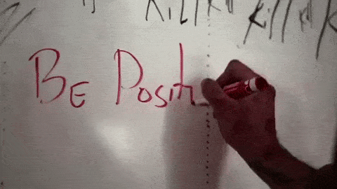 A person writing be positive on a whiteboard