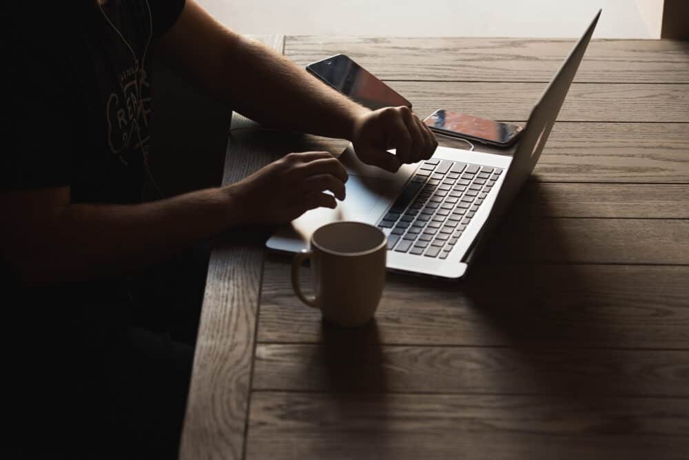 Hands typing on laptop on desk with coffee mug