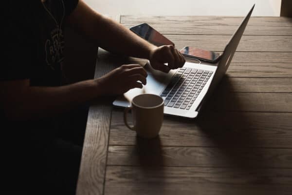 Hands typing on laptop on desk with coffee mug