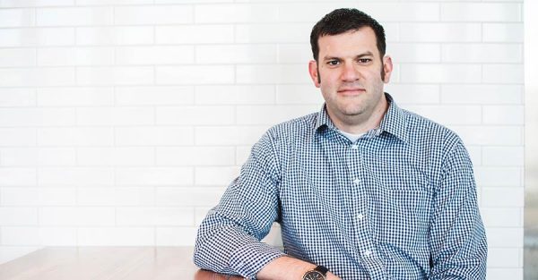 Man in blue shirt sitting at table in front of white subway tile wall