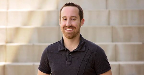 Man in black polo standing in front of tan brick wall