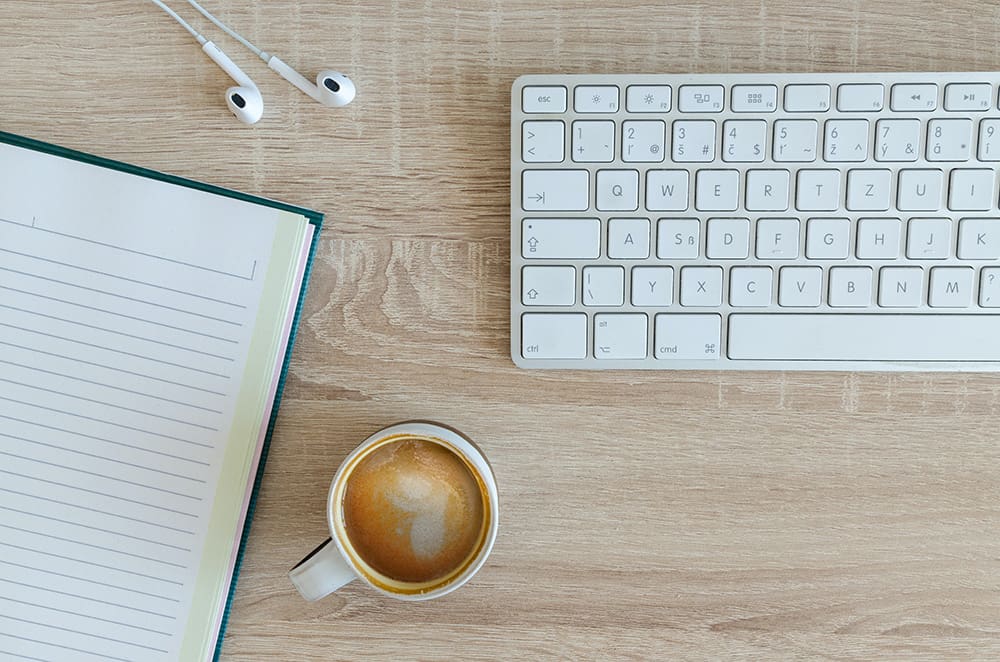 White keyboard on desk with coffee, headphones, and notebook