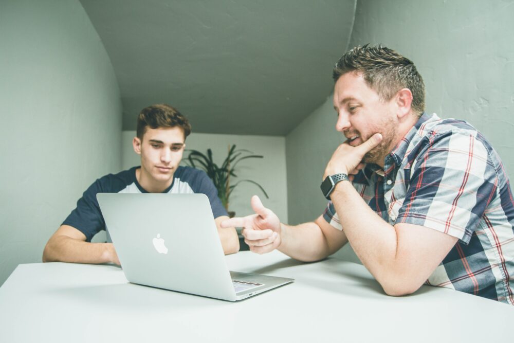 man wearing white and black plaid button-up sports shirt pointing the silver MacBook photo