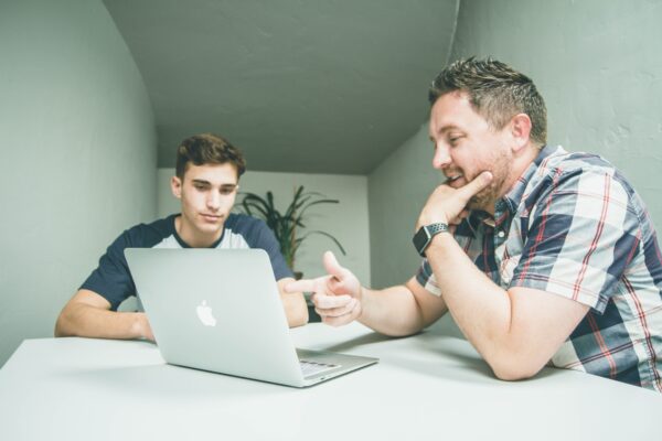 man wearing white and black plaid button-up sports shirt pointing the silver MacBook photo