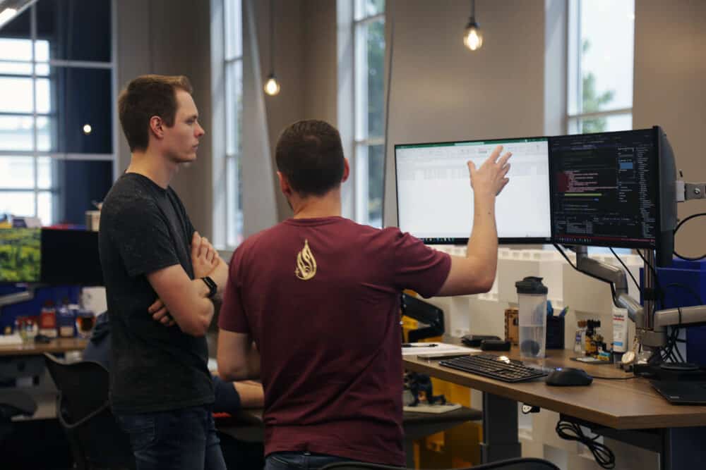 Two men facing computer screens talking