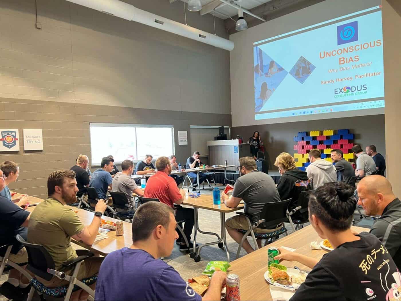 People sitting at desks eating lunch and watching a presentation