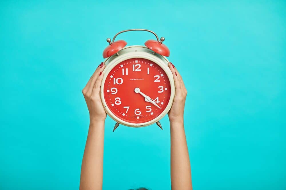 Hands holding a red alarm clock on blue background