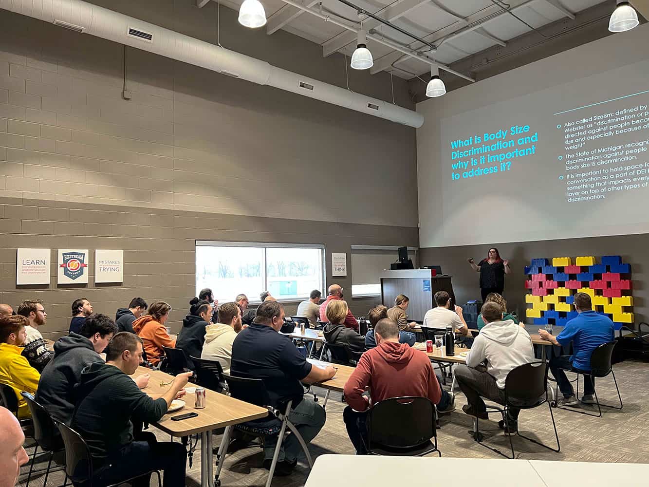 People sitting at desks eating lunch and watching a presentation