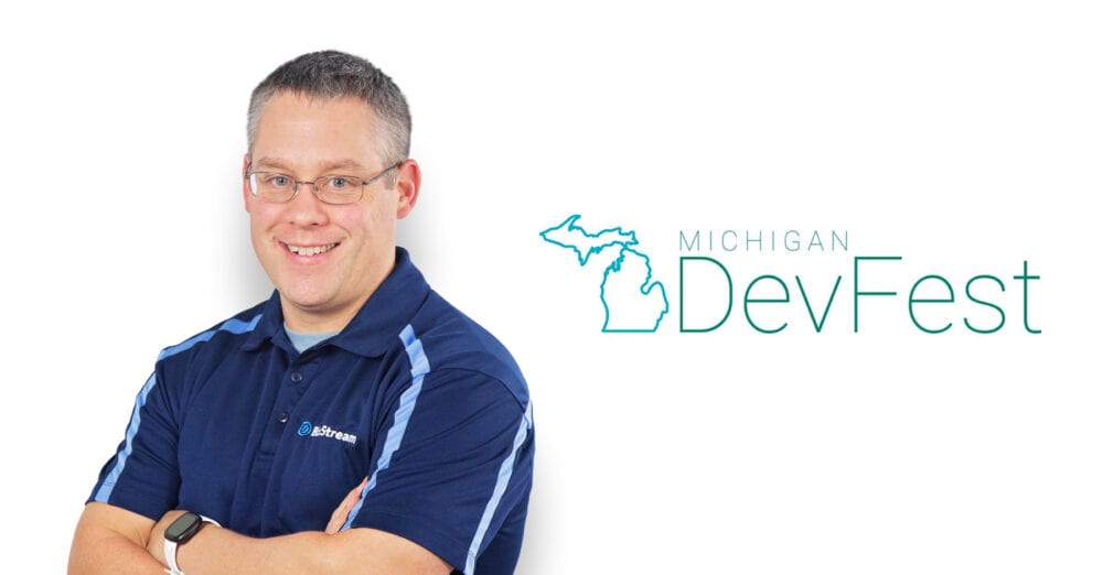 Man in blue polo shirt with arms crossed smiling next to a Michigan DevFest logo