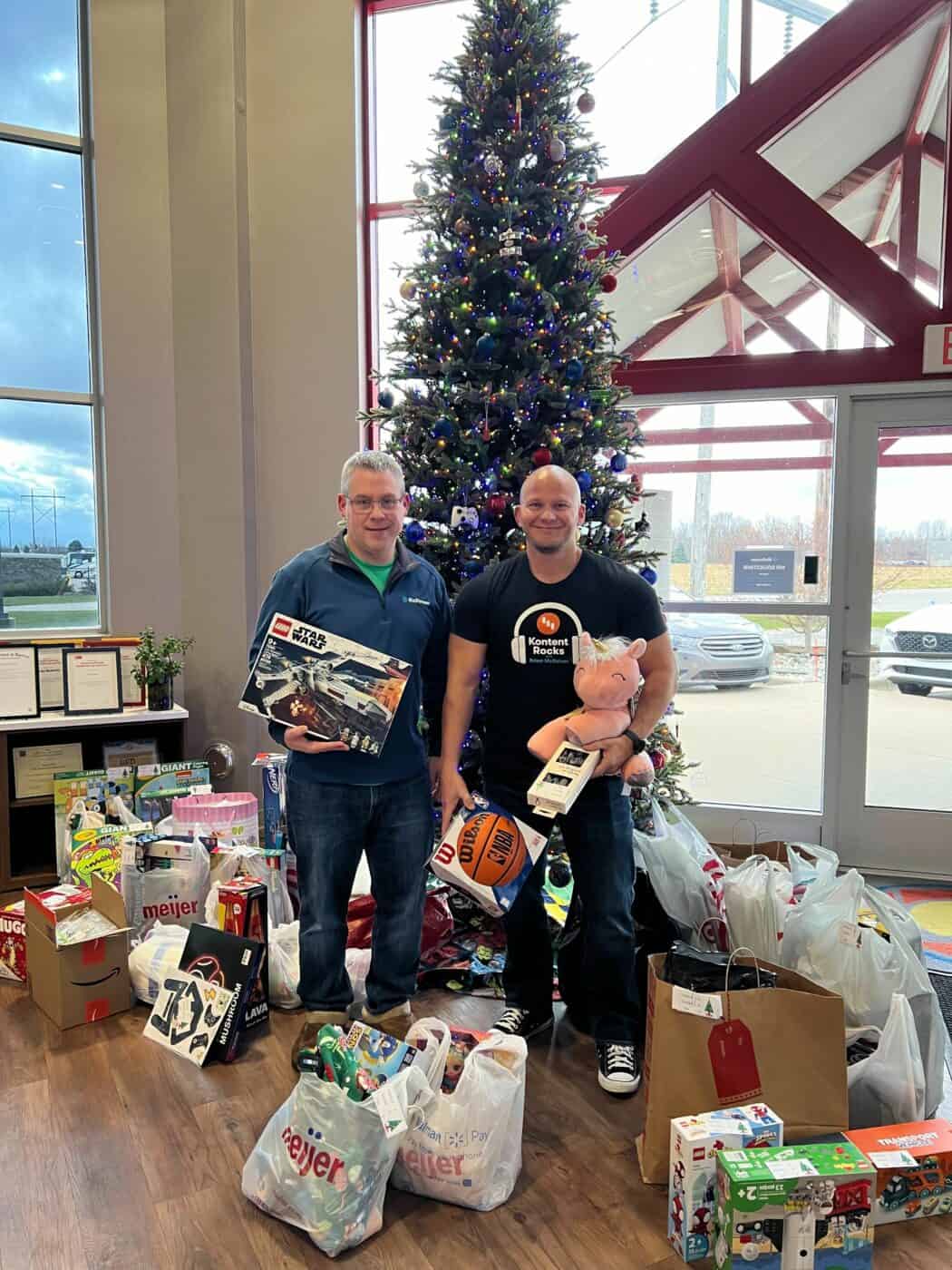 Two men holding Christmas gifts in front of a Christmas tree