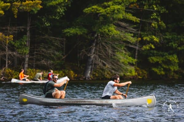 Two people canoeing on a river with trees in the background