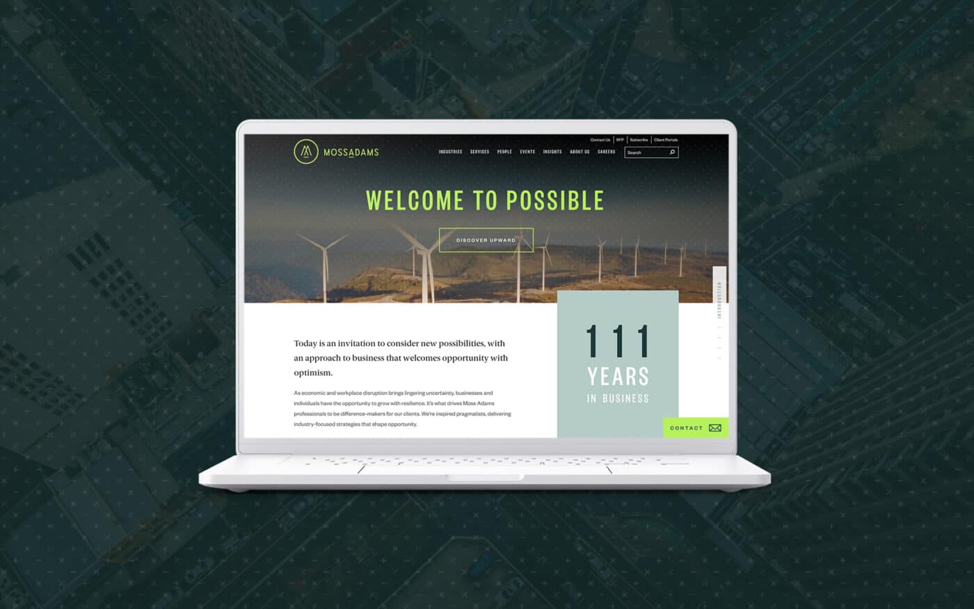 A laptop displaying the Moss Adams website on its screen, with the Moss Adams logo and navigation menu at the top. The website features a hero banner with the text "WELCOME TO POSSIBLE" above an image of wind turbines in a scenic landscape. Below the banner, there's a section highlighting "111 YEARS IN BUSINESS" in large text. The overall theme of the website conveys a professional and optimistic approach, using a combination of green and white colors. The laptop is set against an aerial view of an urban intersection with a dark, textured overlay.
