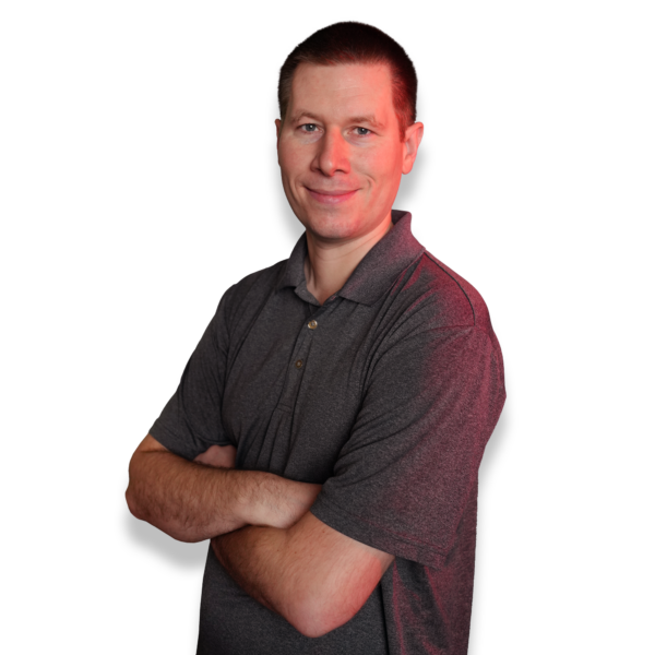Person with short dark hair, wearing a gray polo shirt, standing confidently with arms crossed against a black background, with a subtle red lighting effect on one side.