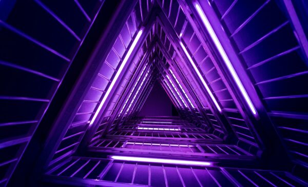 Geometric triangular tunnel with glowing purple neon lights, creating a futuristic and symmetrical visual effect with metallic railings and a sense of depth.