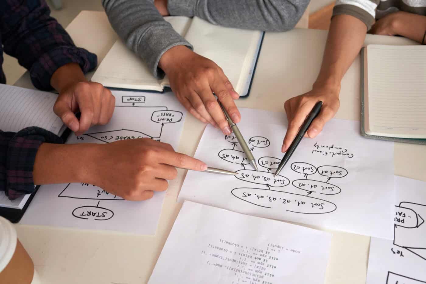 Hands of programmers discussing algorithm, view from above