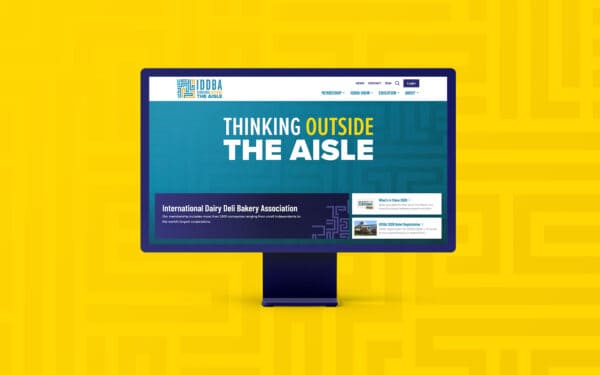 Desktop monitor mockup featuring the full IDDBA homepage layout, including navigation, hero messaging, and featured content cards.