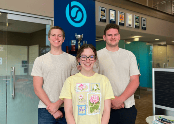 BizStream's three Summer 2026 Interns, Mason Compston, Maggie McKeiver, and Joseph Heinz, smiling together in the BizStream office lobby in front of the company logo.