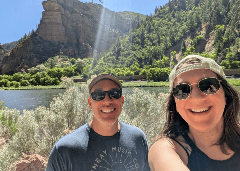 Drew and Jordan smiling outdoors during a community hike at the 2026 CSAE Annual Conference in Glenwood Springs, Colorado, with river and canyon landscape in the background.