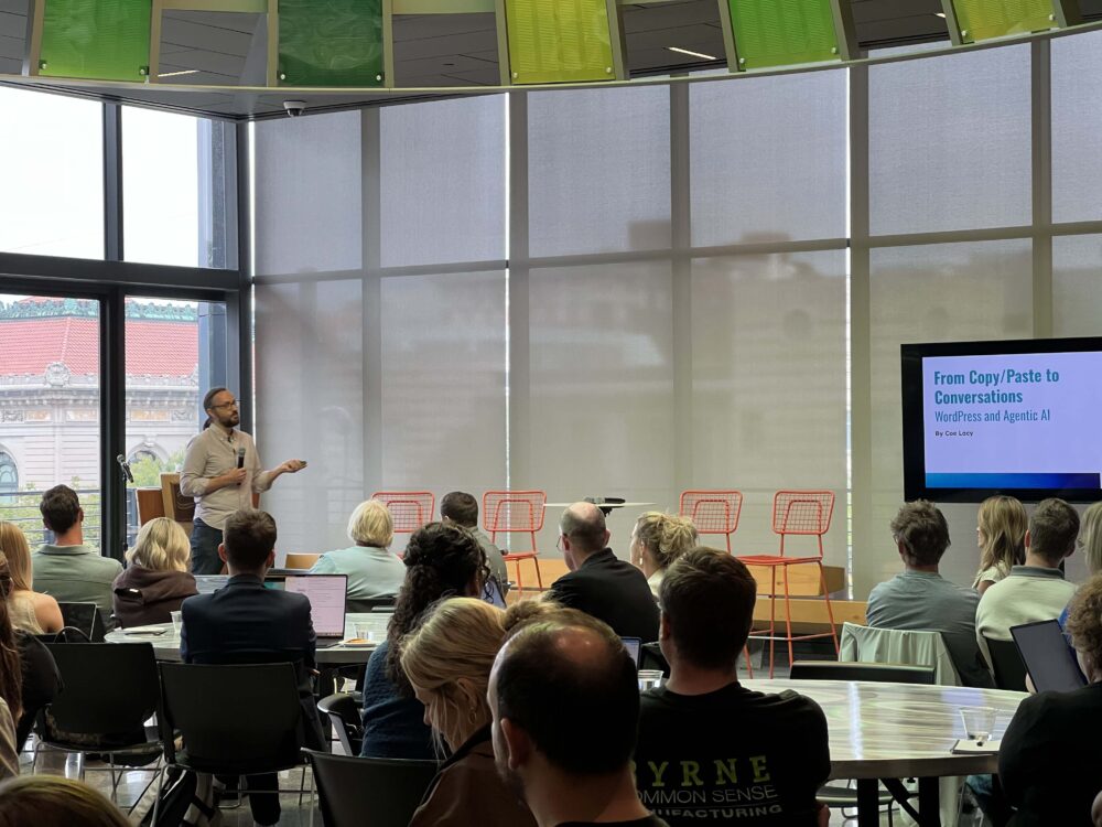 Coe Lacy speaks to a seated audience next to a slide reading "From Copy/Paste to Conversations: WordPress and Agentic AI" during BizStream's session at Tech Week Grand Rapids.
