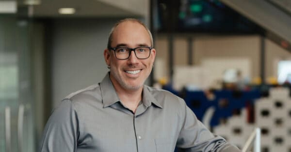Smiling professional man in office with computers and tech equipment.